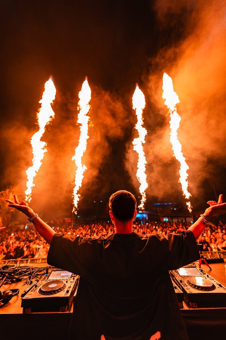 Un DJ abre los brazos ante el público y cuatro columnas de fuego.