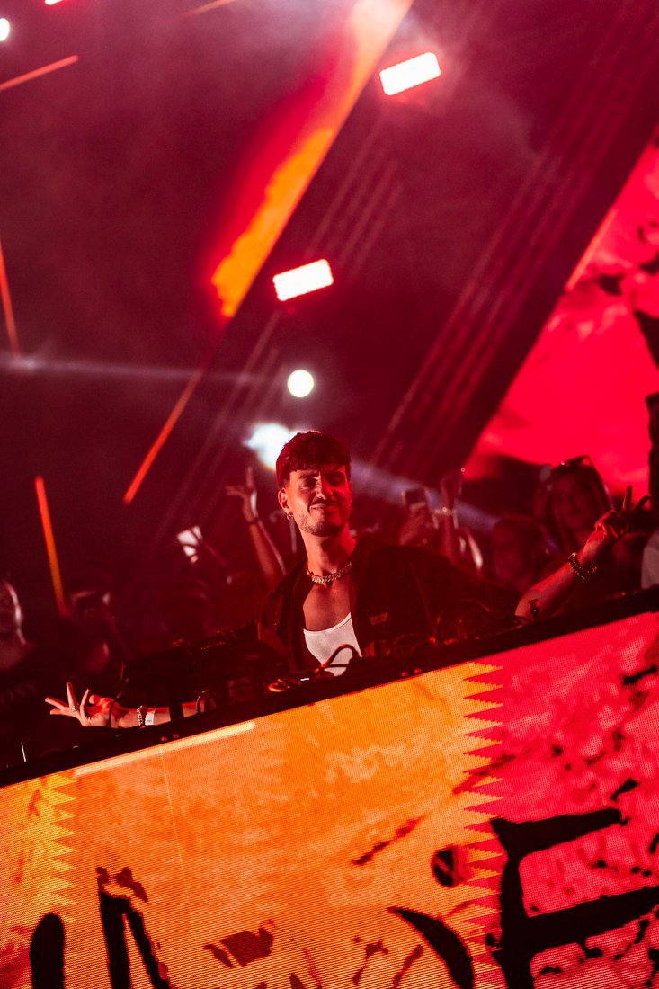 Un DJ junto a la pantalla de la cabina, iluminada en rojo y naranja.
