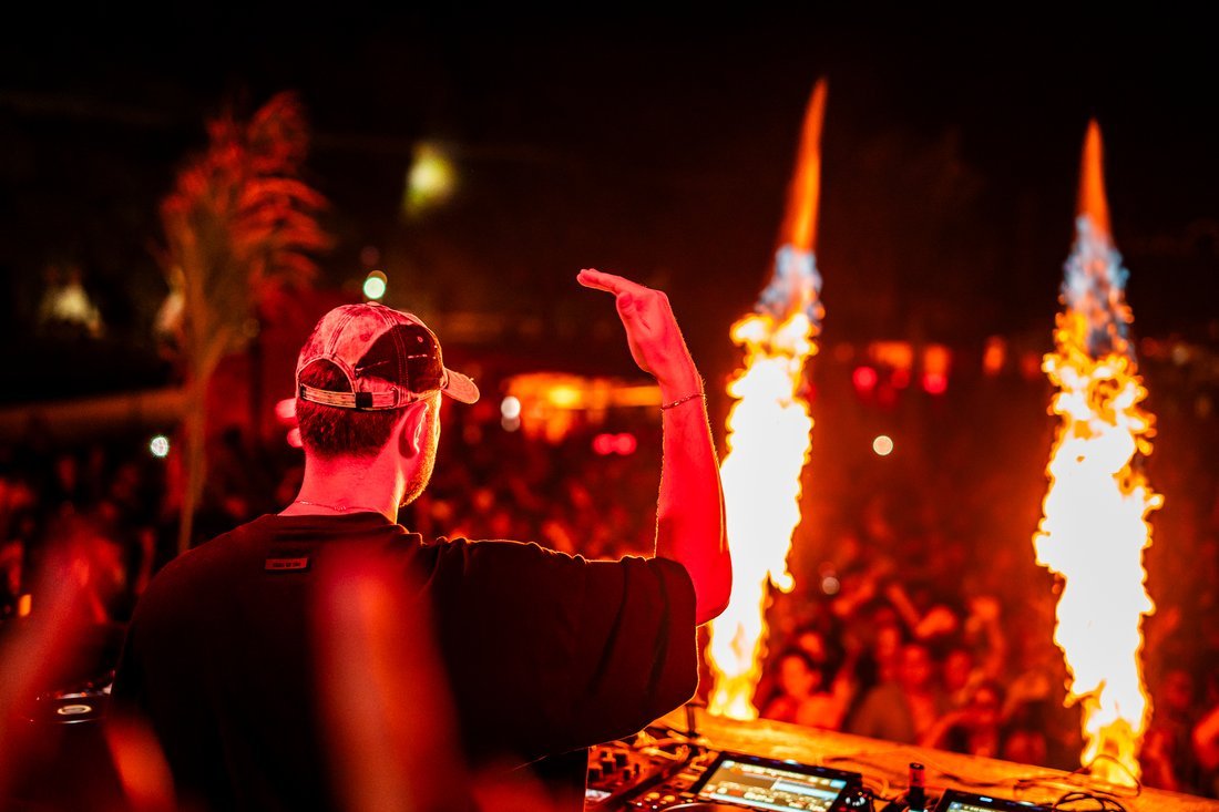 Vista desde la cabina de un DJ frente al público y dos columnas de fuego.